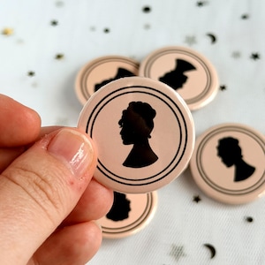 Op de afbeelding: Een set ronde buttons met een lichtroze achtergrond en een zwarte silhouet van een persoon in profiel. Elke button is versierd met een dubbele zwarte cirkelvormige rand. Het ontwerp is consistent op alle ronde buttons in deze afbeelding.