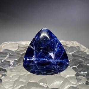 May include: A deep blue, triangular cabochon gemstone with white veining. The stone is polished and has a smooth, glossy finish.