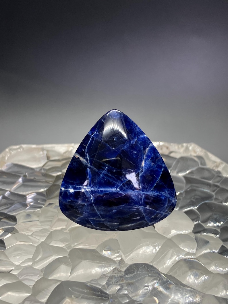May include: A deep blue, triangular cabochon gemstone with white veining. The stone is polished and has a smooth, glossy finish.