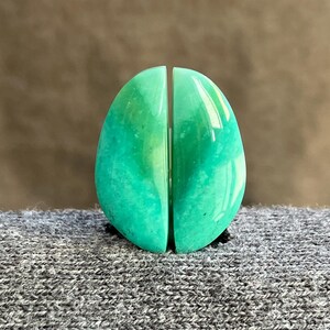 Peut inclure: Objet décoratif ovale en deux parties, dans des tons de vert. Les pièces sont séparées par un petit espace vertical. L'objet a une finition brillante et polie et repose sur une surface grise texturée. Le fond est marron uni.