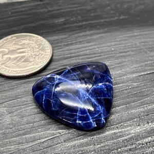 May include: A triangular blue and white gemstone with a smooth, polished surface. The gemstone has a marbled pattern with white veins running through the blue.