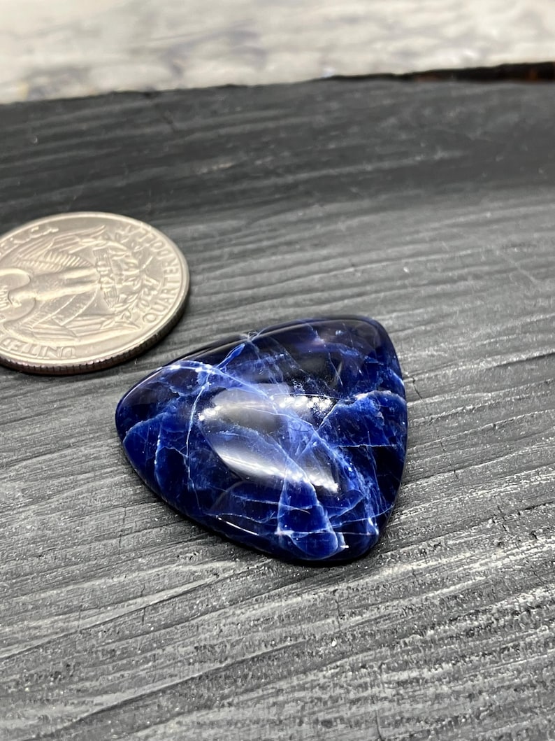 May include: A triangular blue and white gemstone with a smooth, polished surface. The gemstone has a marbled pattern with white veins running through the blue.