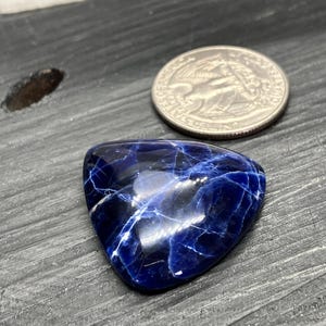 May include: A triangular blue and white cabochon gemstone with a marbled pattern. The gemstone is approximately the size of a UK 20 pence coin.