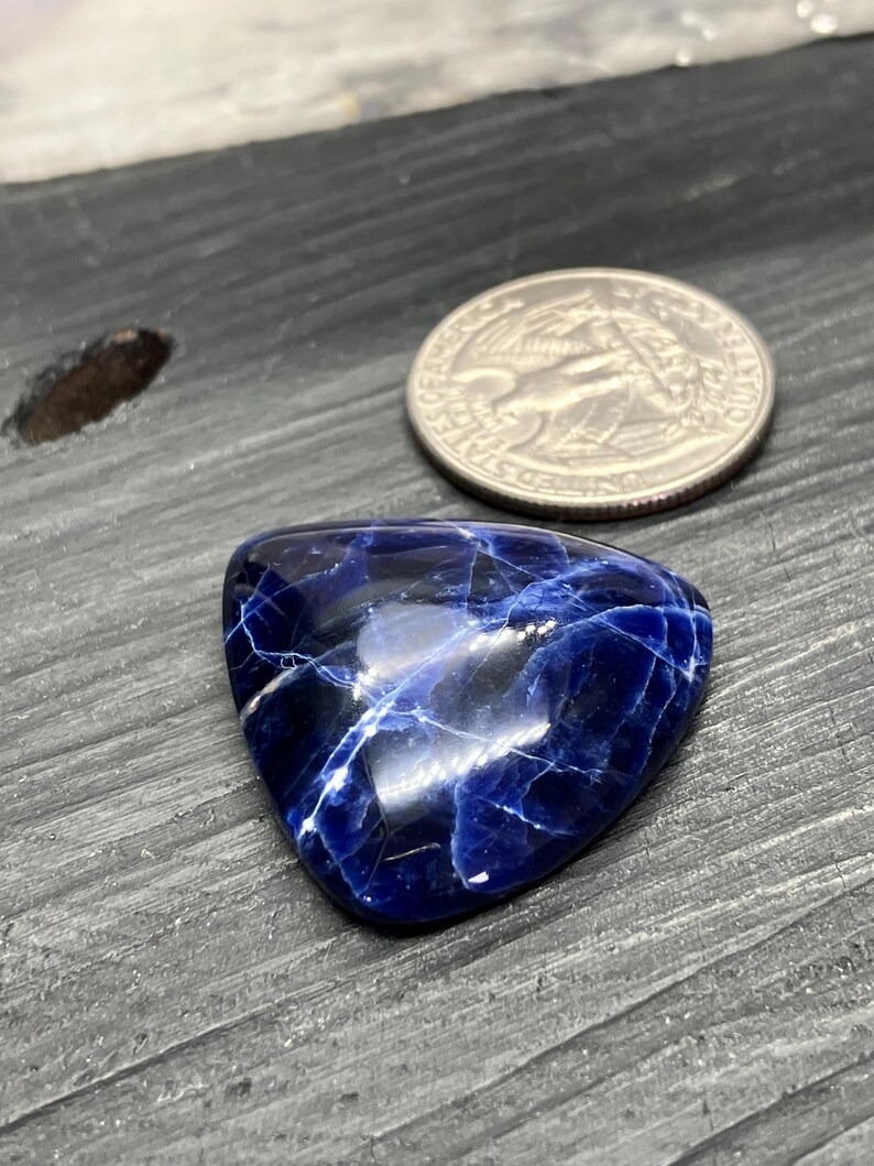 May include: A triangular blue and white cabochon gemstone with a marbled pattern. The gemstone is approximately the size of a UK 20 pence coin.