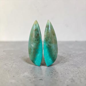 May include: Two polished, teardrop-shaped gemstones. They display a gradient of colours, from vibrant turquoise at the base to green and brown at the top. The gemstones are set against a neutral background. Each stone is approximately 4 cm in length.