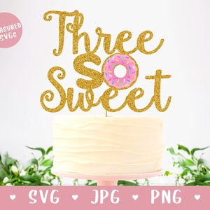 Op de afbeelding: Gouden glitter taarttopper met de tekst "Three So Sweet" en een roze en witte donut met sprankjes.