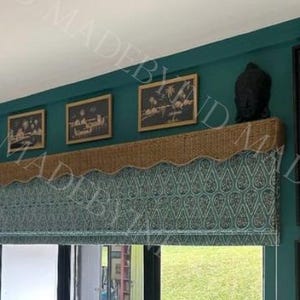 May include: A room with teal walls, featuring a woven lampshade, a patterned window shade, and framed artwork. The window shade has a teal and white paisley design. A decorative shelf holds a black sculpture and framed pictures.