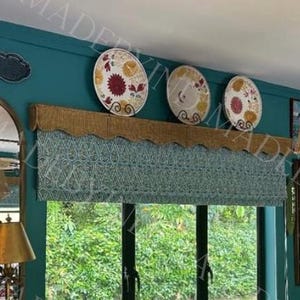 May include: An arched, gold-framed mirror is the focal point, complemented by decorative plates and a woven lampshade. The room features a teal wall, a window with a patterned valance, and a decorative antler display. The overall theme is eclectic.