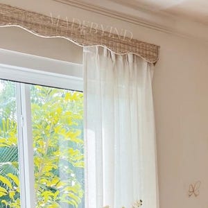 K&ouml;nnte beinhalten: Eine helle Holzkommode mit sechs Schubladen und runden Kn&ouml;pfen steht unter einem Fenster mit wei&szlig;en Vorh&auml;ngen. Eine gerippte wei&szlig;e Vase mit wei&szlig;en Blumen steht darauf. Drei kleine Schmetterlings-Wanddekorationen sind an der beigen Wand.