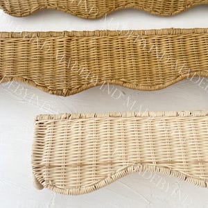 K&ouml;nnte beinhalten: Drei rechteckige Wandregale aus geflochtenem Rattan mit gewelltem Rand. Die oberen zwei Regale haben einen mittelbraunen Farbton, w&auml;hrend das untere Regal eine hellere, nat&uuml;rliche Cremefarbe aufweist. Jedes Regal zeigt ein enges Webmuster.