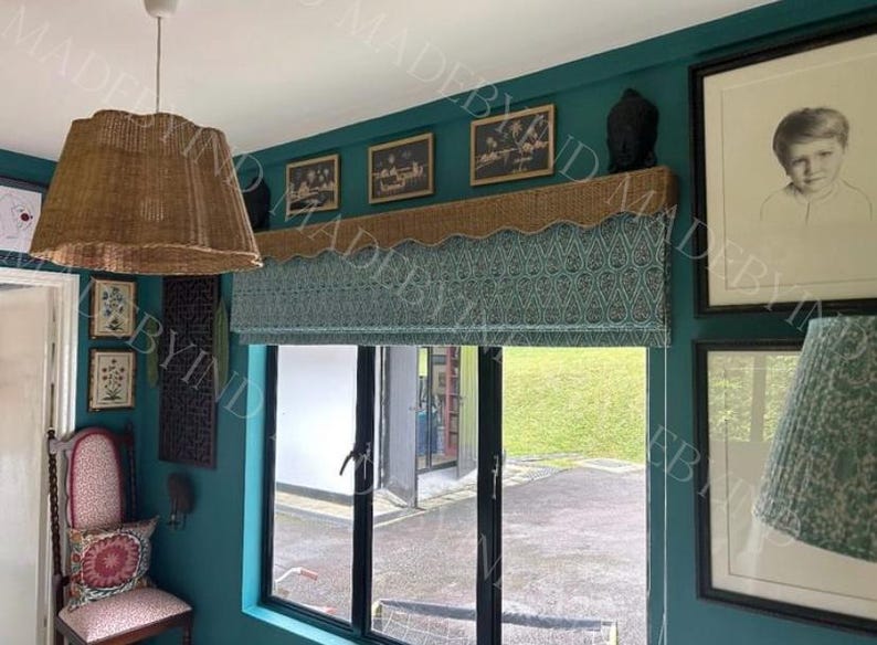 May include: A room with teal walls, featuring a woven lampshade, a patterned window shade, and framed artwork. The window shade has a teal and white paisley design. A decorative shelf holds a black sculpture and framed pictures.