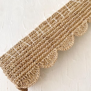 May include: A close-up of a brown, woven trim with a scalloped edge. The trim has a white thread running through it.
