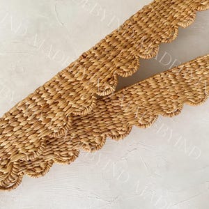 Peut inclure: Deux bandes décoratives tressées à bords festonnés de couleur beige naturel. Les bandes sont faites de fibres étroitement tissées, créant une surface texturée. Le design suggère un article d'artisanat ou de décoration intérieure.
