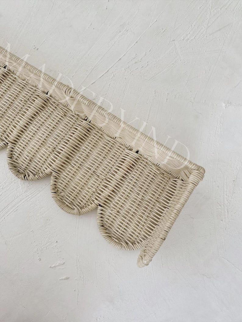 Puede incluir: Un estante de pared de rat&aacute;n tejido en color beige claro con un borde superior recto y un borde inferior festoneado decorativo. El estante tiene una textura natural y un patr&oacute;n semicircular en la parte inferior, hecho de material de junco fino.
