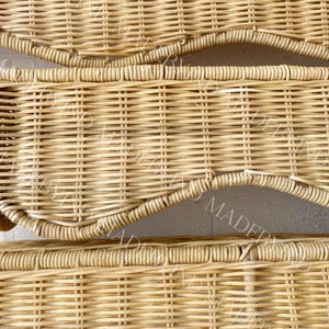 K&ouml;nnte beinhalten: Ein hellbraunes, geflochtenes Weidenpaneel mit einem sich wiederholenden horizontalen Muster und geschwungenen, wellenf&ouml;rmigen Kanten. Das Material besteht aus d&uuml;nnen, naturfarbenen Ruten, die eng miteinander verflochten sind und eine strukturierte Oberfl&auml;che bilden.