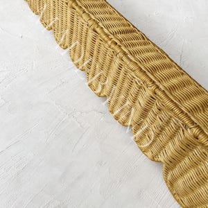 Puede incluir: Una bandeja rectangular larga de mimbre con un acabado natural en color marr&oacute;n claro y un dise&ntilde;o de borde festoneado decorativo a lo largo del lateral. La textura tejida es uniforme en toda la pieza, mostrando un patr&oacute;n de espiga detallado.