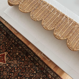 Puede incluir: Un cenefa rectangular de mimbre tejido con un borde inferior festoneado. El material natural de color marr&oacute;n claro est&aacute; estrechamente entrelazado en un patr&oacute;n repetitivo, creando una pieza decorativa texturizada con un dise&ntilde;o ondulado.