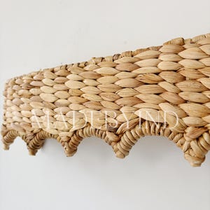 Puede incluir: Estante tejido de fibra natural con borde festoneado. El estante está hecho de material marrón claro, tejido apretado y presenta el texto "MADEBYIND". Diseñado para montaje en pared.