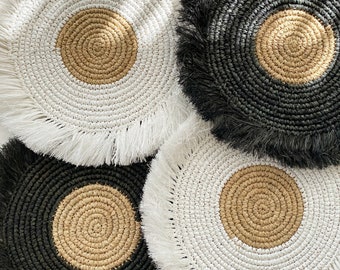 Pode incluir: Três peças redondas de decoração de parede tecidas com uma borda de franja. O centro de cada peça é um círculo menor de material tecido em cor natural. Os círculos exteriores são preto, branco e preto.