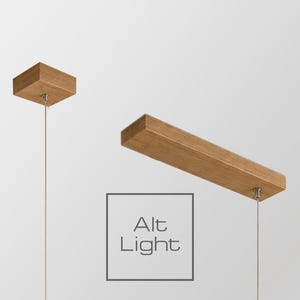 May include: A light fixture featuring a rectangular wooden beam suspended by thin metal cables from a square wooden ceiling canopy. The wood has a natural grain finish. The text Alt Light is printed in a gray square box below the beam.
