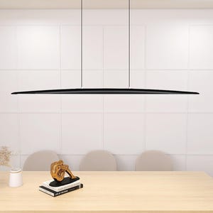 May include: A black linear pendant light fixture hangs from the ceiling above a wooden table with three chairs. The light fixture is long and thin, with a slightly curved shape. The table is made of light wood and has a smooth surface. The chairs are upholstered in a light beige fabric.
