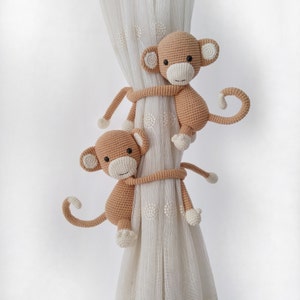 Peut inclure: Deux attaches de rideaux en forme de singe en crochet de couleur brun clair. Les singes sont accrochés à un rideau blanc transparent à petits pois blancs.
