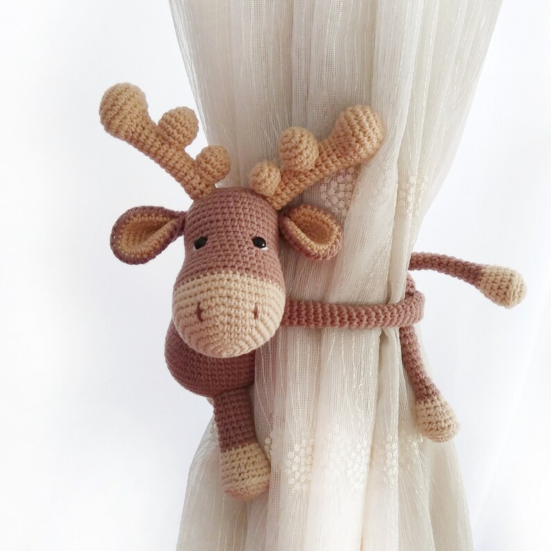 May include: A brown crocheted reindeer with a long tail used as a curtain tieback. The reindeer has a brown body with beige antlers and a beige face.