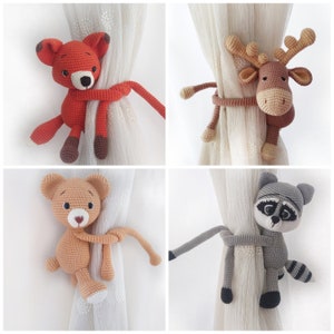 May include: Four crocheted animal curtain tiebacks. The tiebacks are in the shape of a fox, a reindeer, a bear, and a raccoon. The tiebacks are all holding onto a curtain with their arms and legs.