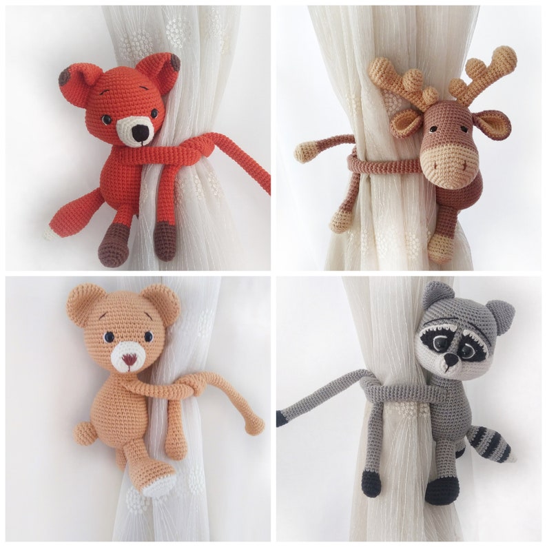 May include: Four crocheted animal curtain tiebacks. The tiebacks are in the shape of a fox, a reindeer, a bear, and a raccoon. The tiebacks are all holding onto a curtain with their arms and legs.