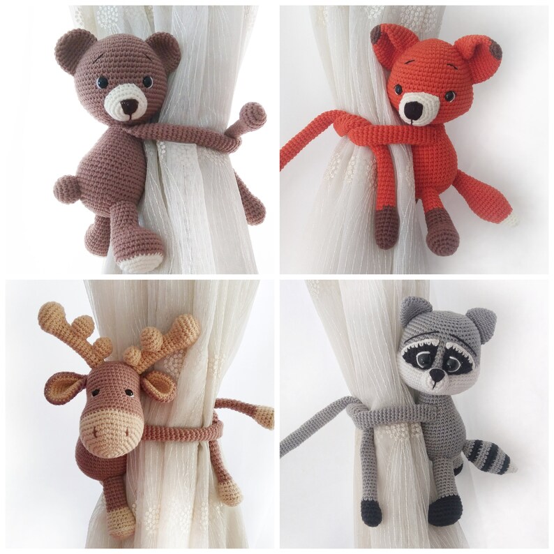 May include: Four crocheted animal curtain tiebacks. A brown bear, an orange fox, a brown reindeer, and a gray raccoon. Each animal is holding a loop of yarn to tie back curtains.