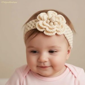May include: A cream-colored crochet headband featuring a large, layered flower embellishment at the center. The flower is accented with small, round, off-white beads in the middle. The headband has a textured, open-weave pattern throughout.