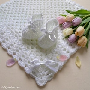 Può includere: Una coperta per neonati bianca all'uncinetto con scarpine abbinate e un nastro bianco. Un bouquet di tulipani colorati e petali sparsi aggiungono un tocco di colore. La coperta e le scarpine sono fatte a mano.