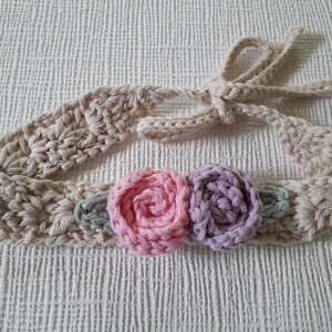 May include: A beige crocheted headband with a pink and purple flower embellishment.