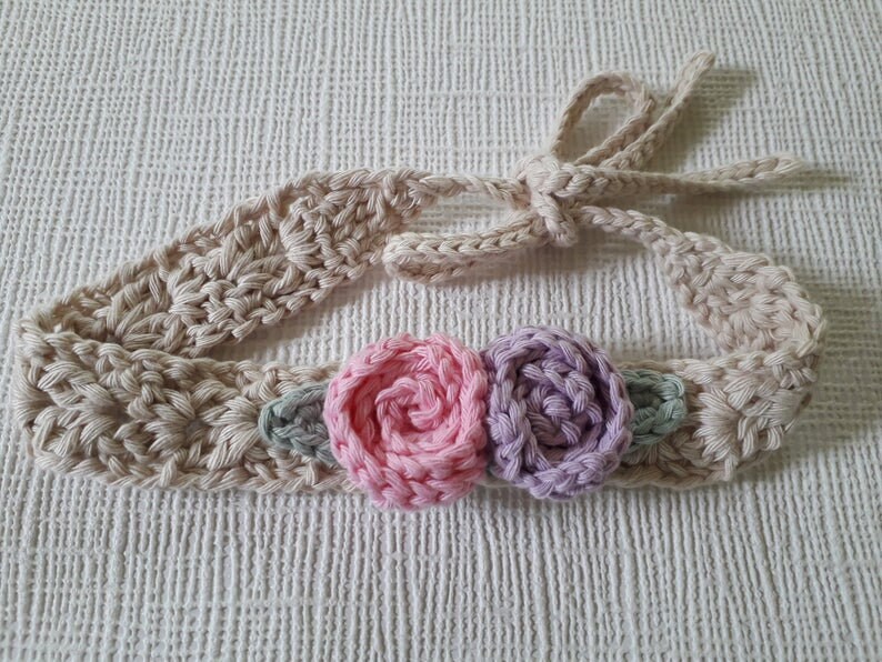 May include: A beige crocheted headband with a pink and purple flower embellishment.
