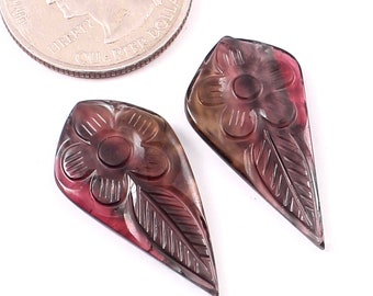 May include: Two carved gemstone pendants in the shape of a leaf with a flower design. The pendants are a mix of brown, pink, and purple.