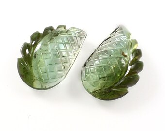 May include: Two green carved gemstone pineapple pendants. The pendants are carved with a pineapple design and have a green and clear color.