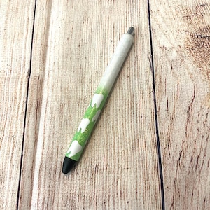 May include: A white and green pen with a black tip and a design of white teeth on a green background.