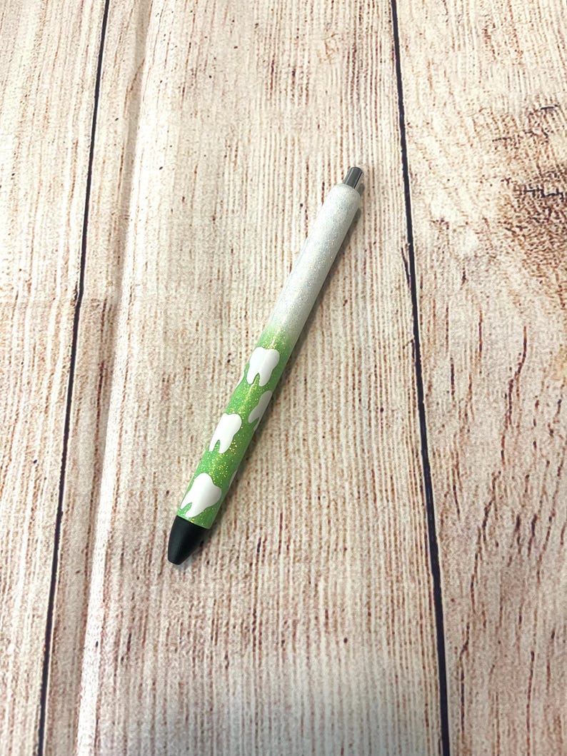 May include: A white and green pen with a black tip and a design of white teeth on a green background.