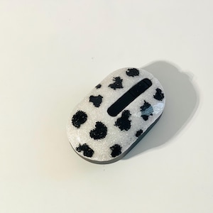 May include: A white wireless computer mouse with a black cow print design. The mouse has a black scroll wheel and a black button on the top.