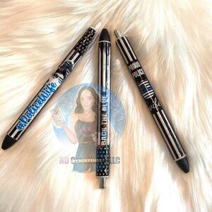 May include: Three black and silver pens with different designs. The first pen has a blue and white American flag design with the text "Back the Blue" on it. The second pen has a blue and white thin blue line design with the text "Proud Police Wife" on it. The third pen has a blue and white thin blue line design with the text "#PoliceWife" on it.