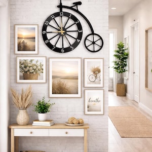 May include: A decorative wall arrangement featuring a black bicycle-shaped clock with gold hands, surrounded by framed landscape art and a console table with decor. The wall is white brick. The word "breathe" is in a framed print.