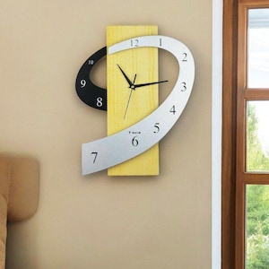 May include: Modern wall clock with a unique design. The clock features a yellow rectangular base with a black and silver curved design. The clock hands are black, and the numbers are in a modern font.