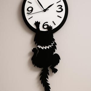 May include: A black and white wall clock with a whimsical design. The clock face is white with black numbers and hands. A black silhouette of a creature hangs from the clock, adding a playful touch to the decor.