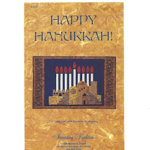 May include: A card with a gold background and a blue and red illustration of a menorah with candles. The text "HAPPY HANUKKAH!" is at the top of the card. The text "Copyright 1999 Elizabeth Rosenberg" is at the bottom of the card. The text "Inventing Tradition" is below the copyright information. The text "2888 Hemlock Street" is below the company name. The text "Yorktown Heights, NY 10598" is below the street address. The text "914-962-7238" is below the city and state.