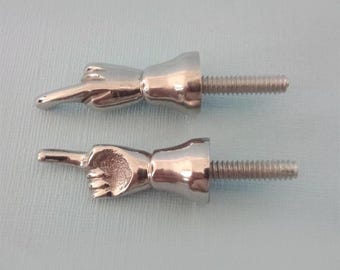 May include: Two silver-colored cabinet knobs shaped like hands pointing. Each knob has a threaded bolt for attachment. The knobs are on a light blue background. These unique knobs add a playful touch to furniture.