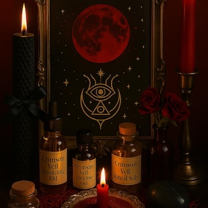 May include: A still-life arrangement featuring a framed print of a red moon and celestial symbols. Bottles of oil and ritual salt are displayed with lit candles and red roses. The labels read "Crimson Veil".