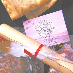 May include: A rolled up scroll with a white feather and red ribbon, a pink card with the text "Litha Blessings" and a drawing of a woman with a sun behind her, and a clear glass ornament with colorful glitter inside.