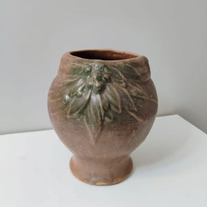 May include: A brown ceramic vase with a green floral design. The vase has a rounded body and a flared base.