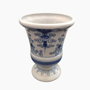 May include: White ceramic vase with blue floral patterns. The vase has a wide rim and a pedestal base. The blue design features swirls and stylized floral motifs. The vase is suitable for displaying flowers or as a decorative item.