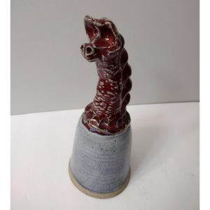 May include: A ceramic bell with a red, textured dragon head and a blue and white glazed base.